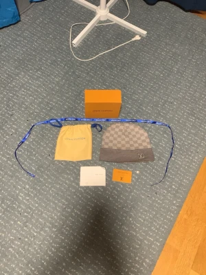 Louis Vuitton grå mössa med schackmönster - Exklusiv grå mössa från Louis Vuitton med klassiskt schackmönster och LV-logga framtill. Mössan är stickad och kommer box o påse o tags 