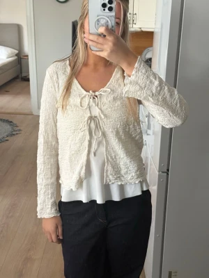Krämvit kofta med knyt - Säljer en jättefin krämvit kofta med strukturerat tyg och två knyt framtill. Koftan har v-ringning, långa ärmar💞