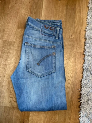 Dondup jeans  - Dondup jeans som sitter slim (George/ritchie) Säljer ett par ljusblå jeans med klassisk femficksdesign och snygga kontrastsömmar. Jeansen har en patch med detaljer vid linningen och är tillverkade i mjukt denimtyg. Perfekta för en avslappnad och trendig look.