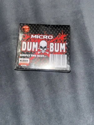 Micro Dum Bum fyrverkeripetarder - Micro Dum Bum är en ask med små fyrverkeripetarder från Klásek Pyrotechnics. Asken är svart med röd och vit text samt en dödskalle på framsidan. Produkten är avsedd för utomhusbruk och innehåller flera smällare.