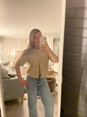 Beige kortärmad kofta med pärlknappar - Söt beige kofta med korta ärmar och pärlknappar framtill. Koftan har en rak passform och är stickad i ett mjukt material som ger en avslappnad men ändå chic look. Perfekt att styla med jeans eller kjol för en trendig outfit.