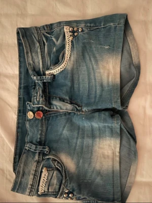Blå jeansshorts med spetsdetaljer - Säljer ett par ljusblå jeansshorts från Lantie med snygga slitningar och dekorativa spetsdetaljer vid fickorna. Fint skick och pris kan diskuteras 💞