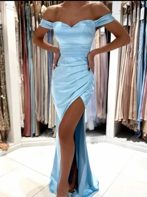 Klänning från Dressroom Linné - Snygg ljusblå långklänning med offshoulder. Klänningen har en slits framtill och figurnära passform. Tillverkad i silkes material. Perfekt för bal eller festliga tillfällen.