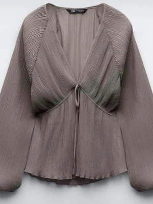 Plisserad taupe blus från Zara - Trendig taupefärgad blus från Zara med plisserat tyg och djup v-ringning. Blusen har långa, vida ärmar och knytning framtill som ger en snygg siluett. Tillverkad i ett lätt, flowy material som ger en cool och avslappnad vibe.