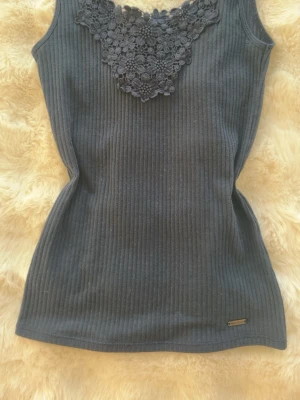 Marinblå ribbad linnetopp från Hollister  - Snygg marinblå ribbad linnetopp med blommig spetsdetalj vid halsen. Har en bra passform. Perfekt att styla med jeans eller kjol. Jag köpte den för 240kr ny 