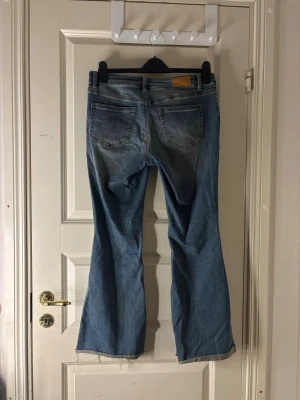 Blå bootcut jeans från Vero Moda - Säljer ett par blå bootcut jeans från Vero Moda med klassisk femficksdesign och råa, avklippta benslut. Jeansen har en snygg tvättad look och är tillverkade i denim. Perfekta för en avslappnad och trendig stil. De är kortare då jag klippt dem (jag är 155cm lång)