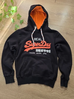 Superdry vintage hoodie - Supersnygg svart vintage Superdry hoodie. Lappen med storleken är avklippt, så jag vet inte exakt vad det är för storlek. Dock är den 58 cm lång och 49 cm bred vilket ChatGPT säger motsvarar Small, eller en liten Small. Mycket bra skick på varan! 