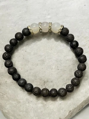 Armband med Svarta lavastenar  med vita agat stenar - Snyggt armband med svarta lavapärlor och tre vita, halvgenomskinliga pärlor i mitten. Mellan de vita pärlorna sitter små guldfärgade detaljer som ger extra bling. Perfekt accessoar för dig som gillar stilrena smycken med en twist.