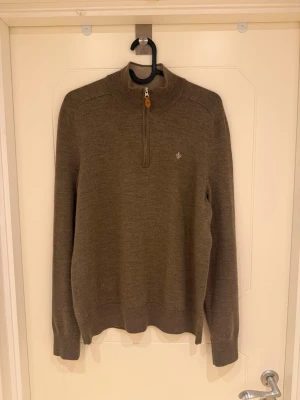Morris Brun/Beige stickad tröja med halvzip - Säljer en brun stickad tröja från Morris med halvzip och diskret logga på bröstet. Tröjan har ett snyggt kabelstickat mönster framtill, ribbade muddar och hög krage. Perfekt för dig som gillar klassisk och stilren design. Tröjan är i 100% merinoull, modell 185cm & 82kg.