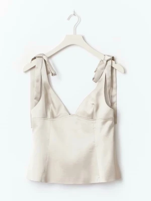 Beige linnetopp med knytband - Supersnygg beige linnetopp med breda axelband som knyts i rosetter. Toppen har en v-ringad urringning och är figurnära med en lätt croppad passform. Perfekt att styla med jeans eller kjol för en trendig look.