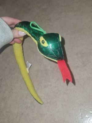 Grön och gul ormsvans till maskerad - Mjukisdjur orm i grönt tyg med gul undersida och röd tunga. Materialet är mjukt och stoppat. Inga defekter