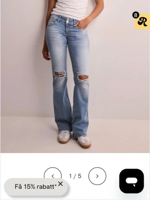 Ljusblå bootcut jeans med slitningar - Säljer ett par ljusblå bootcut jeans med slitna hål över knäna och snygga fickdetaljer bak med knappar. Jeansen har hög midja och klassisk femficksmodell. Perfekta för en avslappnad och trendig look.