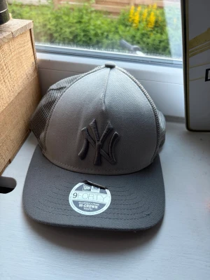 Grå New Era Yankees keps - Snygg grå keps från New Era med New York Yankees-logga framtill. Modellen är 9FORTY med böjd skärm och mesh på sidorna för extra ventilation. Justerbar baktill för perfekt passform. Perfekt för dig som gillar sportig och avslappnad stil.