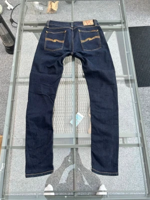 Nudie Jeans Skinny Lin – Dry Deep Orange, 31/32 - Säljer mina Nudie Jeans i modellen Skinny Lin. Det är en riktigt snygg modell i tvätten "Dry Deep Orange" som ger en perfekt mörk och stilren look.  Modell: Skinny Lin (smal passform/skinny fit).  Storlek: W31 L32.  Material: 99 % ekologisk bomull och 1 % elastan, vilket ger både kvalitet och lite stretch för bra komfort.  Skick: Mycket fint begagnat skick. Perfekta jeans för dig som letar efter kvalitet och en snygg passform som håller länge. Skicka ett meddelande om du har några frågor!