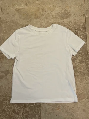 Vit basic t-shirt i bomull - Enkel och stilren vit t-shirt med rund hals och korta ärmar. Tillverkad i mjuk bomull som känns skön mot huden. Perfekt att matcha med jeans eller shorts för en clean look.