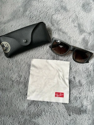 Svarta Ray-Ban solglasögon Wayfarer - Klassiska svarta Ray-Ban Wayfarer solglasögon med mörka glas. Säljes med original svart fodral i skinn och putsduk med Ray-Ban-logga. Perfekt accessoar för dig som vill ha en tidlös och ikonisk look.