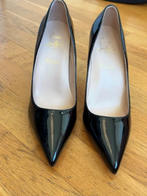 Svarta lackpumps från Louboutin - Snygga svarta pumps i lack från Christian Louboutin med klassisk spetsig tå och ikonisk röd sula. Skorna har en elegant siluett och hög klack, perfekta för att lyfta vilken outfit som helst. Tillverkade i glansigt läder och kommer med originalpåse.