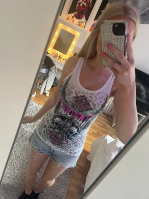 Vit linne med tryck och leopardmönster - Säljer ett vitt linne med coolt tryck i svart, rosa och grått samt diskret leopardmönster upptill. Linnet är ärmlöst och har en tight passform. Perfekt för dig som gillar edgy och unika plagg.