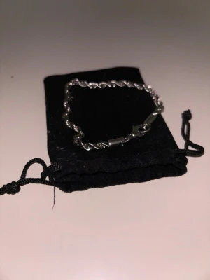 Snyggt Cordell silverfärgat armband - Stilrent armband i silverfärg med tvinnad kedja och klassiskt lås. Kommer med en svart tygpåse för förvaring. Perfekt accessoar för att lyfta din outfit med en enkel men elegant touch. Rostfritt stål (4 mm, 20 cm)