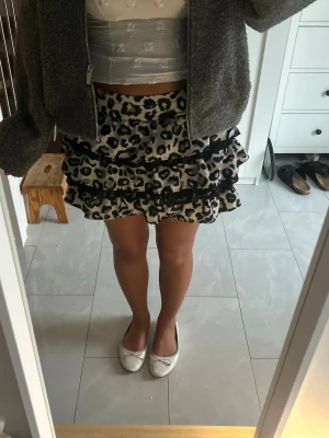 Leopardmönstrad volangkjol - Säljer en kort kjol med leopardmönster och flera volanger. Kjolen har svarta spetsdetaljer mellan volangerna och är i en beige och svart färgskala. Perfekt för dig som vill sticka ut med en trendig och lekfull stil. Den är i barnstorlek men skulle säga att den sitter som en S.