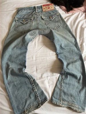 True Religion ljusblå bootcut jeans joey super T - Säljer ett par ljusblå jeans från True Religion med bootcut passform och slitna detaljer vid benslut.  Lite sliten, priset kan sänkas vid snabb affär 