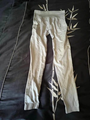 Beige höga träningsbyxor med ribbad midja - Säljer ett par beige träningsbyxor med hög midja och ribbad kant upptill. De är långa och har en tight passform som framhäver benen. Materialet känns mjukt och stretchigt, perfekt för en chill och snygg look. Aldrig använt bara provat