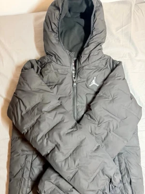 Jordan Puffer Jacket - Säljer en stilren och varm Jordan vinterjacka i svart. Jackan har en klassisk puffer-design med huva, diskret Jumpman-logga på bröstet och en modern passform som passar både till vardags och streetwear.  ✔ 100 % äkta Jordan ✔ Varm vaddering för kalla dagar ✔ Fast huva med mjukt innerfoder ✔ Dragkedja framtill ✔ Sidofickor ✔ Tidlös svart färg som passar till allt ✔ Bekväm och funktionell design  Jackan är i fint skick och fungerar perfekt som vardagsjacka under höst och vinter. En populär modell 