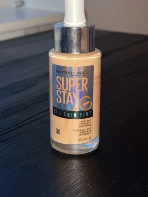 Maybelline Super Stay Skin Tint 36 - Maybelline Super Stay 24H Skin Tint i nyansen 36 med vitamin C. Flytande foundation i glasflaska med pipett, ger en naturlig finish och lång hållbarhet. Perfekt för dig som vill ha lätt täckning och glow.