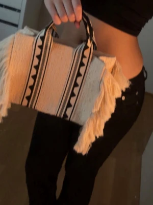H&M strandväska / handväska med fransar - Jättefin jacquard-vävd väska från H&M. Väskan är helt oanvänd. Mycket rymlig med dragkedja på innerficka för småsaker. Perfekt som sommar eller strandväska!