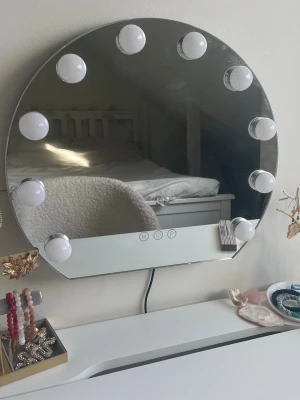 Rund sminkspegel med LED-belysning - Snygg rund sminkspegel med inbyggd LED-belysning runt kanten. Spegeln har touchknappar för att justera ljusstyrkan och är perfekt för sminkning eller styling. Modern design i silverfärgat glas och vit plast. Kan hängas på väggen och kopplas in med sladd.