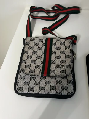 Guc och ci  - Snygg axelväska från Guc och ci i beige canvas med klassiskt GG-mönster och gröna/röda ränder. Väskan har justerbar axelrem i tyg och lock med magnetknäppning. Perfekt för dig som gillar streetstyle och vill ha en ikonisk accessoar.
