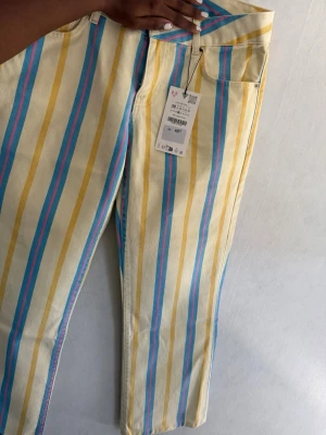 Randiga jeans med pastellfärger - Unika jeans med vertikala ränder i gult, blått och rosa på en ljus bas. Klassisk femficksmodell med hög midja och raka ben. Perfekta för dig som vill sticka ut med färg och mönster. Tillverkade i bomull för skön känsla.
