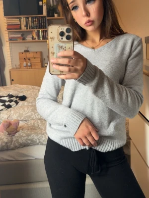 Ljusgrå stickad tröja med V-ringning - Mysig ljusgrå stickad tröja med V-ringad hals och ribbade muddar vid ärmslut och nederkant. Tröjan har en enkel och stilren design som passar perfekt till jeans eller mjukisbyxor. Materialet känns mjukt och behagligt mot huden.