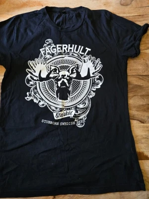 Svart Fagerhult t-shirt med tryck storl S - Cool svart t-shirt från Fagerhult med stort vitt tryck av en älg och texten 'Stubborn Swedish Beer' på framsidan. Klassisk rund hals och korta ärmar. Perfekt för dig som gillar unika motiv och vill sticka ut. Storlek S