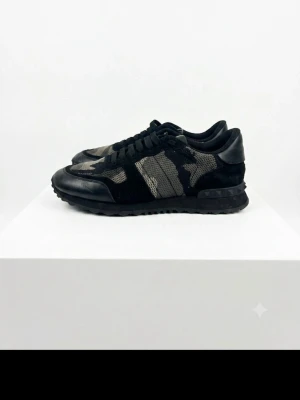 Valentino rockrunners camo - Snygga sneakers från Valentino Garavani med svart och grått camomönster. Skorna har detaljer i mocka och läder, samt svarta snören och sula. Perfekt för dig som gillar streetstyle och exklusiva märken.