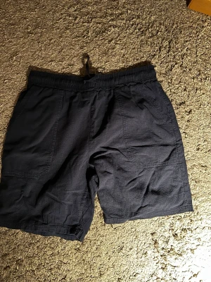 Mörkblå linne shorts med snörning - Säljer ett par mörkblå linne shorts med elastisk midja och snörning. Bra skick och köptes för 200kr och säljes nu för 100kr. Kontakta mig om du har några frågor.