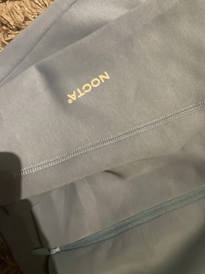 N.O.C.T.A - Snygg ljusblå ziptröja från Nike NOCTA med dragkedja framtill och diskret NOCTA-logga på bröstet. Tröjan har ståkrage med kontrastfärgade detaljer och är tillverkad i mjukt material som känns bekvämt mot huden. Perfekt för en sportig och avslappnad stil.