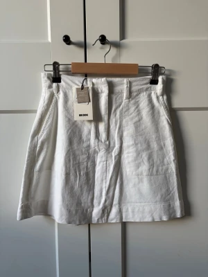 Vit linnekjol från Bik Bok - Fräsch vit kortkjol från Bik Bok i linne med klassisk passform. Kjolen har hällor för bälte och sidfickor, perfekt för en stilren och enkel look. Passar till många olika outfits och är superbekväm under varma dagar. 