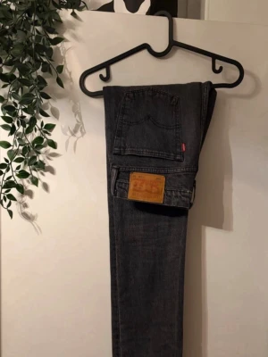 Grå Levi's slim jeans - Säljer ett par grå slim jeans från Levi's med klassisk femficksdesign och den ikoniska läderlappen bak i midjan. Jeansen har en smal passform och är tillverkade i slitstark denim. Perfekta för en avslappnad och trendig look.