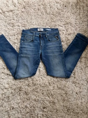 Blå slim fit jeans från Replay - Snygga blå slim fit jeans från Replay med klassisk femficksmodell och snygga slitningar. Jeansen har en brun patch med logga bak i midjan och kontrastsömmar på bakfickan. Perfekta till en avslappnad stil och passar till det mesta.