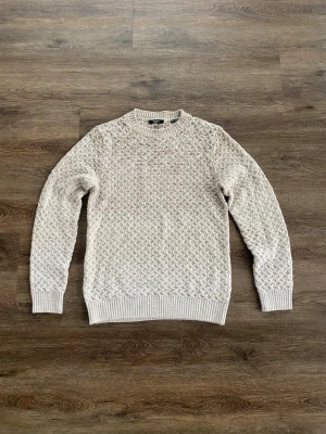 Jack & Jones premium - stl M - Stickad tröja från Jack & Jones i beige nyans med snyggt strukturmönster. Tröjan har rund halsringning och ribbade muddar vid ärmslut och nederkant. Perfekt för lager på lager och ger en avslappnad men stilren look.