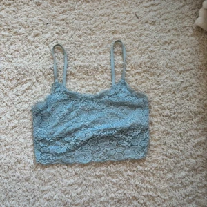 Ljusblå spetsbralette med smala band - Säljer ett ljusblått linne i spets med smala axelband och blommigt spetsmönster. Perfekt för en avslappnad look. Ingen vaddering och croppad modell.