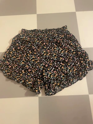 Blommiga volangshorts med resårmidja xxs/xs - Säljer ett par svarta shorts med små blommor i pastellfärger. Shortsen har volangkant och elastisk midja. De är i storlek 146/152 men de är stretchiga så dem passar nog till en xxs/xs😁 Pris kan diskuteras🥰