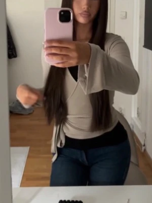 Beige omlottopp med knytband - Säljer en beige omlottopp med långa ärmar och knytband i midjan. Toppen har en v-ringad design och är gjord i mjukt bomullsmaterial. Perfekt att styla med jeans eller kjol för en snygg look.