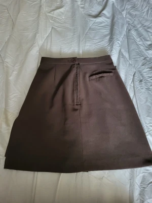 Brun kjol från Röhnisch XS - Snygg brun kjol från Röhnisch i kort modell. Kjolen har en enkel design med knapp och dragkedja framtill samt en liten ficka med logga. Perfekt för dig som gillar stilrena plagg med sportig touch.