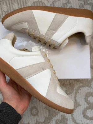 Vita och beige sneakers med gummisula - Snygga sneakers i vitt och beige med klassisk låg siluett. Ovandelen är i en mix av slätt läder och mocka, och skorna har en brun gummisula som ger retrovibbar. Perfekta för dig som gillar stilrena och tidlösa sneakers.