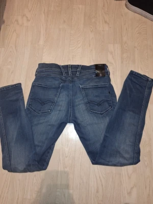 Replay Anbass jeans blå 30/30 - Säljer ett par snygga Replay Anbass jeans i klassisk blå tvätt med coola detaljer på fickorna och bekväm passform. Jeansen har normal midja och raka ben, tillverkade i mjukt bomullsmaterial med lite stretch. Perfekta för dig som gillar stilrena jeans med modern look.