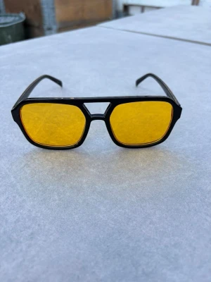 Svarta solglasögon med gula glas - Snygga solglasögon med svart, kantig båge och gula glas. Glasögonen har en retroinspirerad design med breda skalmar och markerad näsbrygga. Perfekta för dig som vill sticka ut med en cool och unik look.🕶️⛱️☀️