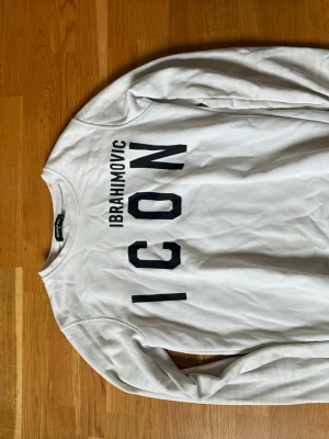 Vit sweatshirt DSQUARED2 ICON - Säljer en vit sweatshirt från DSQUARED2 med svart text 'IBRAHIMOVIC ICON' på framsidan. Tröjan har rund halsringning och långa ärmar. Perfekt för dig som gillar streetwear och vill sticka ut med en ikonisk look.