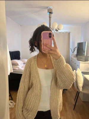 Beige chunky stickad kofta - Mysig beige stickad kofta med oversized passform och grovstickat mönster. Koftan har långa ärmar och en öppen front utan knappar, perfekt att slänga över en topp. Passar dig som gillar en avslappnad och trendig stil.
